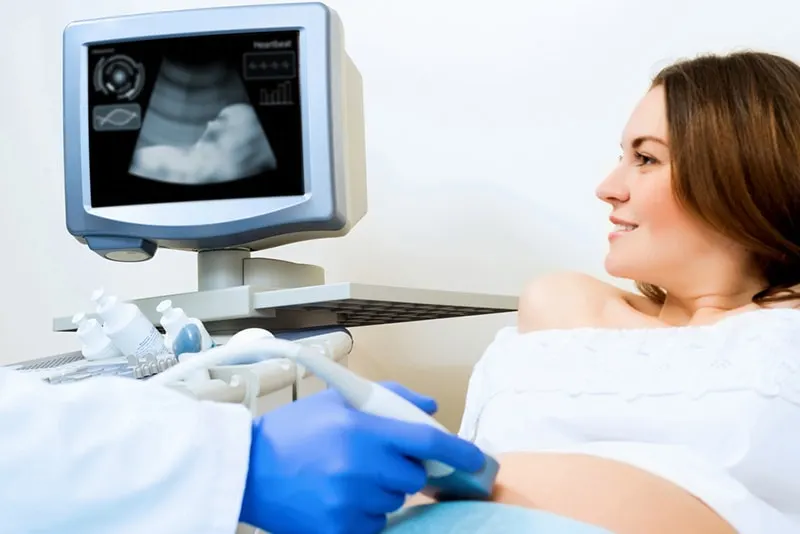 lächelnde junge Frau, die einen Ultraschallbild ihres Babys im Mutterleib in der Klinik erhält