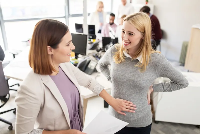 lächelnde schwangere Frau, die mit ihrem Chef im Büro spricht