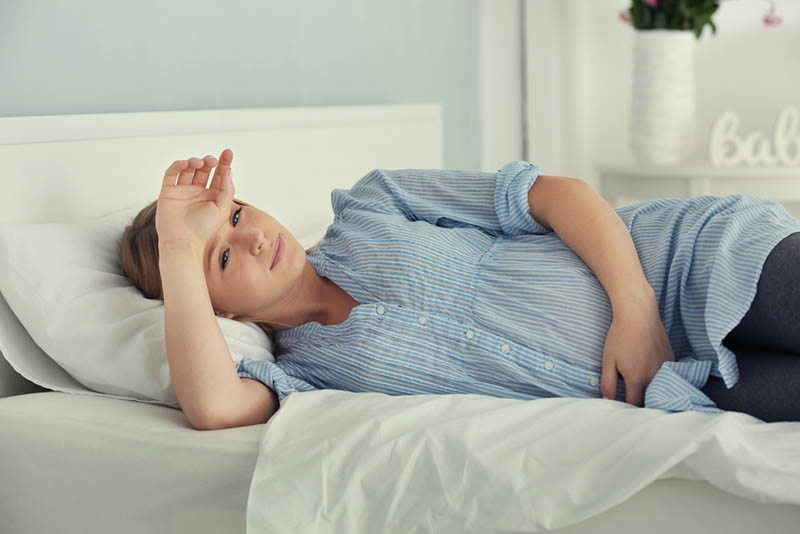 müde schwangere Frau im Bett mit der Hand auf der Stirn liegend