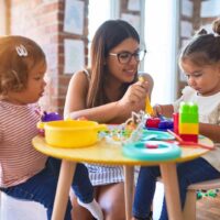 Lehrerin im Kindergarten sitzt mit zwei süßen Mädchen am Tisch