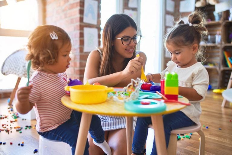 Lehrerin im Kindergarten sitzt mit zwei süßen Mädchen am Tisch