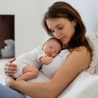 junge Mutter hält schlafendes Neugeborenes im Bett