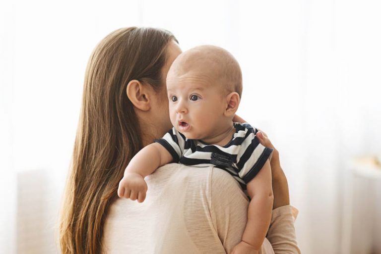 süßes Baby, das Schluckauf hat und von Mutter gehalten wird zu hause