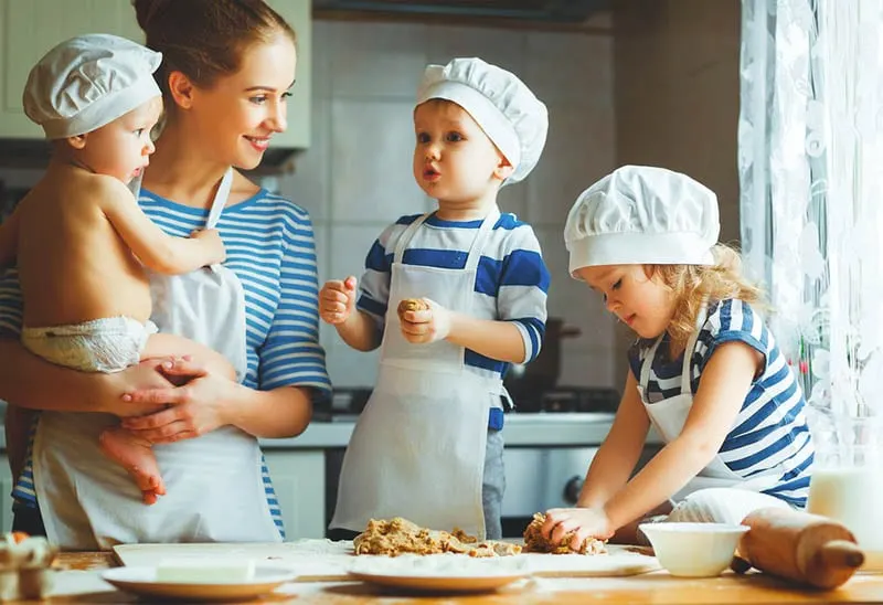 schöne Mutter hält Baby und kocht mit Kindern auf dem Küchentisch