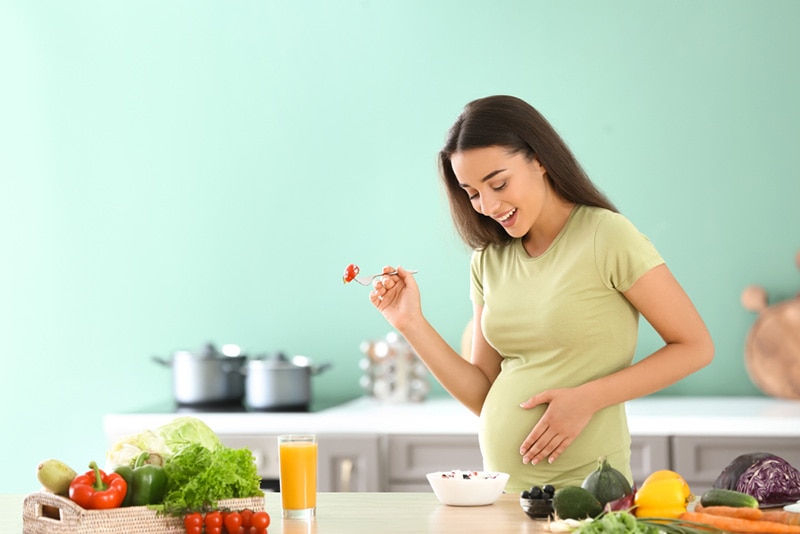 schöne schwangere Frau, die lächelt und gesundes Essen in der Küche isst