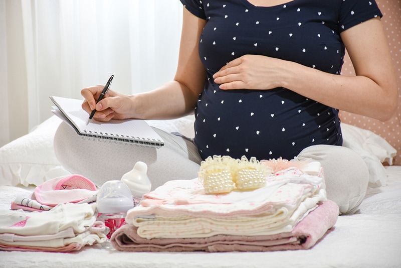 schwangere Frau, die Babyartikel für birt packt und für Organisation aufschreibt