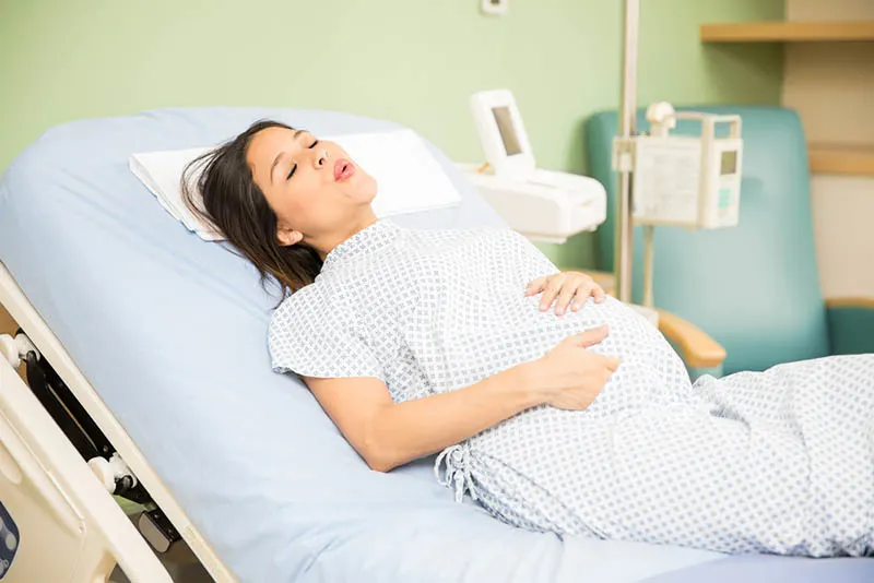 schwangere Frau, die Krankenpflege trägt, die Wehen auf Krankenhausbett hat