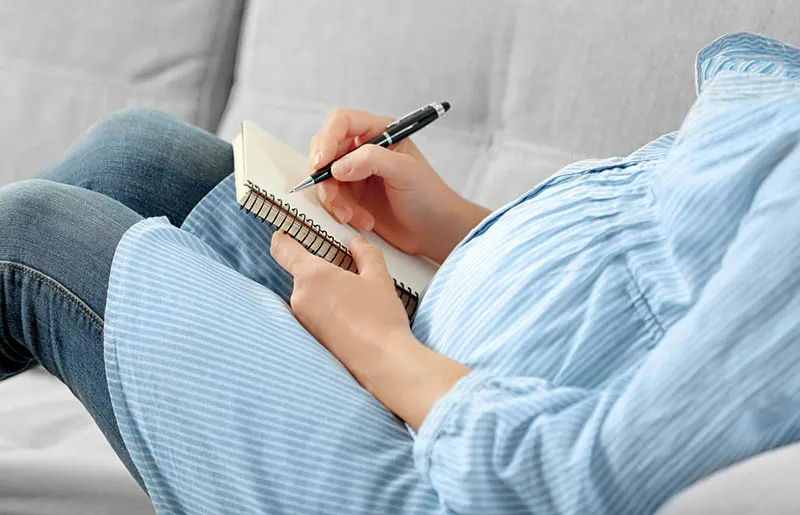 schwangere Frau, die auf der Couch liegt und einen Geburtsplan schreibt
