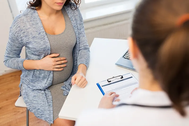 schwangere Frau, die für Bauch hält und mit Arzt über die Hebamme spricht