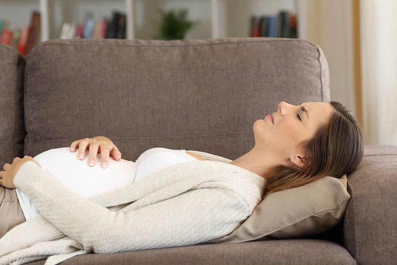 schwangere Frau, die schmerzhafte Kontraktion fühlt und auf der Couch liegt