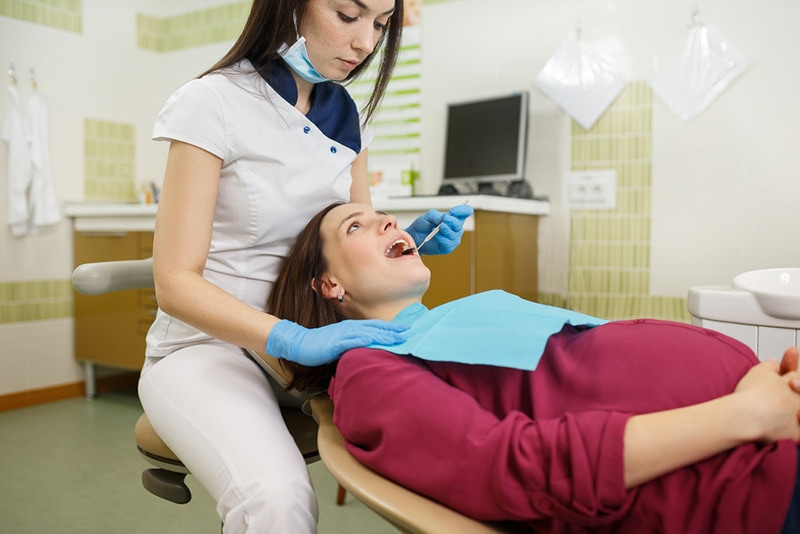schwangere Frau, die still liegt, während Zahnarzt ihre Zähne untersucht