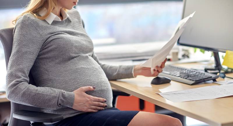  lächelnde schwangere Geschäftsfrau, die am Bürotisch sitzt und Papiere liest