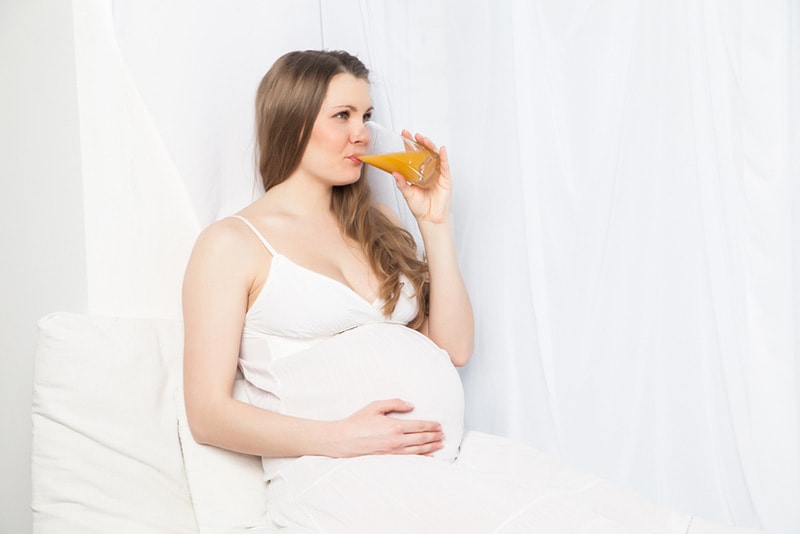 schwangere Frau im weißen Kleid, die Arbeitscocktail trinkt