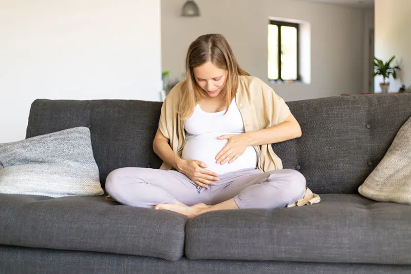 schwangere Frau sitzt auf der Couch und berührt ihren Bauch
