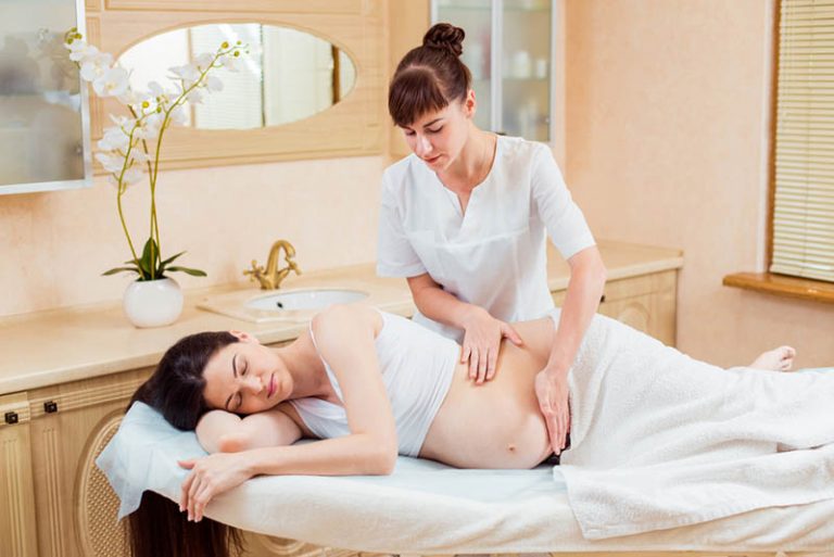 Massagetherapeutin, die einer schwangeren Frau im Spa eine Massage gibt