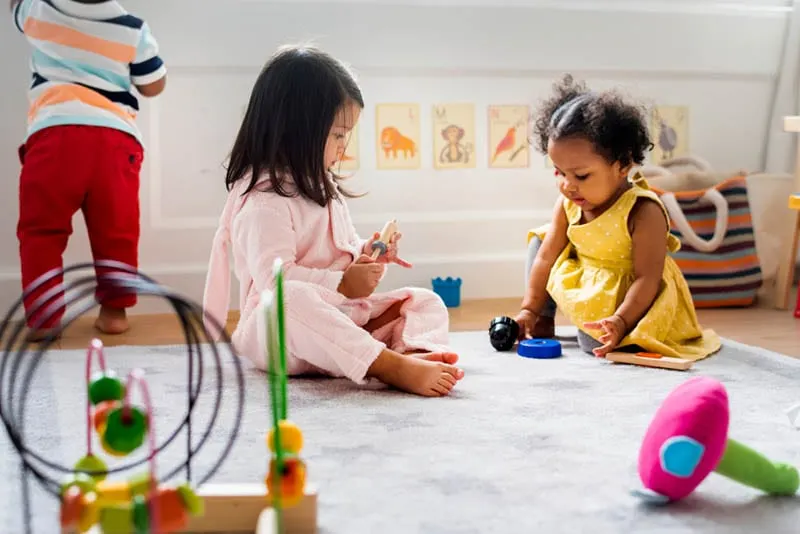 süße Babys spielen auf dem Boden mit Spielzeug im Kindergarten
