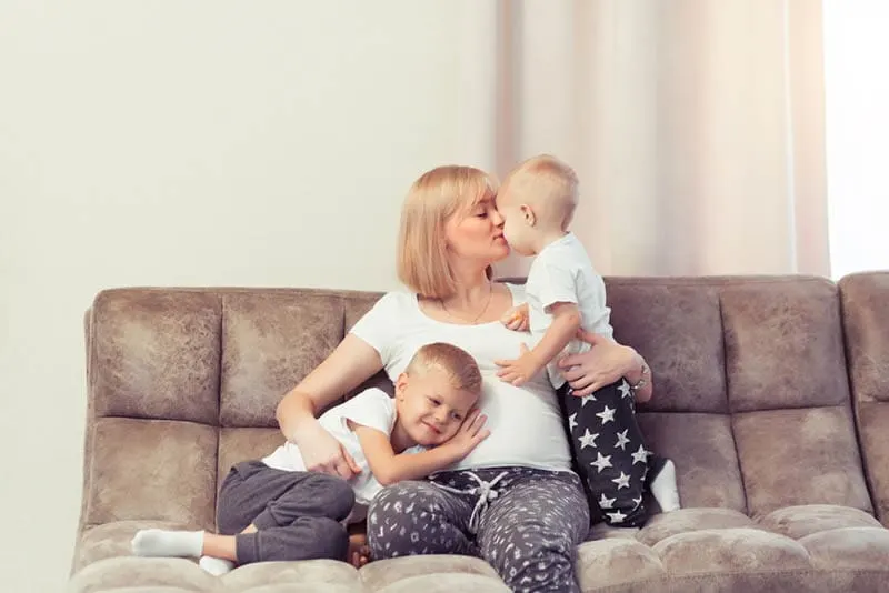 süße schwangere Frau, die mit ihren Söhnen auf der Couch genießt