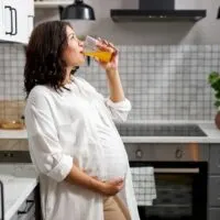schwangere Frau, die Arbeitscocktail in der Küche trinkt