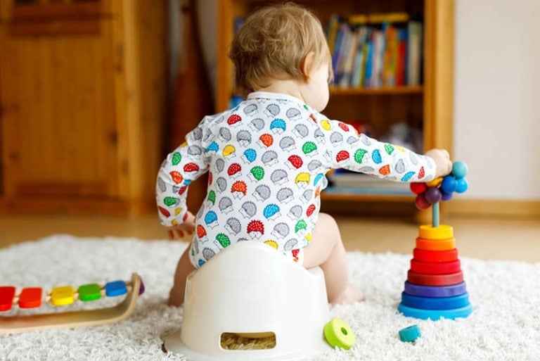 süßes Baby, das auf einem Töpfchen sitzt und mit Spielzeug spielt