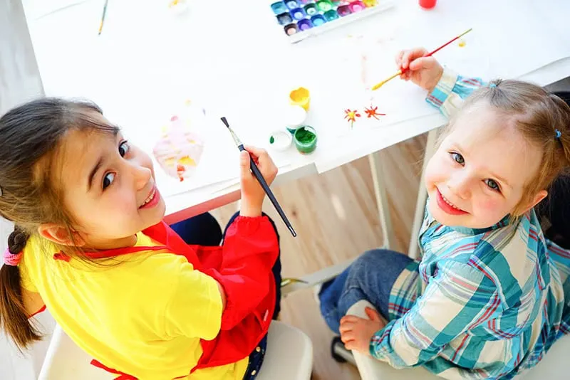 zwei entzückende Mädchen, die Zeichnungen im Kindergarten ausmalen und lächeln
