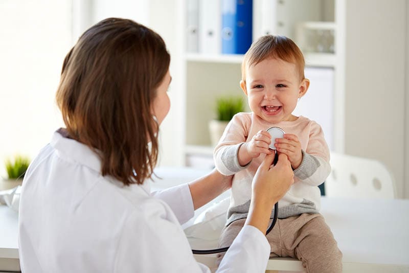 Ärztin untersucht süßes lächelndes Kleinkind auf dem Schreibtisch