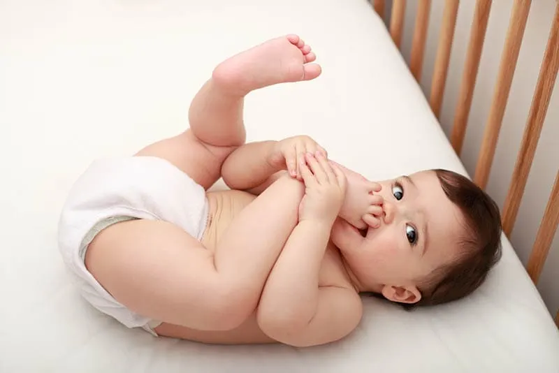 Baby-Junge liegend in der Krippe mit Füßen in den Mund