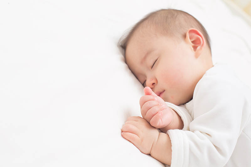 Baby Junge schlafend auf dem Bett mit gekreuzten Händen