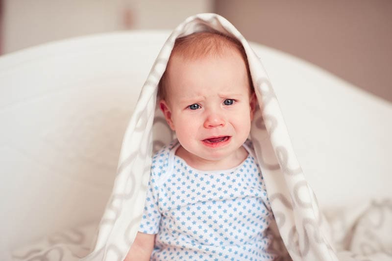 Baby Mädchen weint auf dem Bett mit Babydecke bedeckt