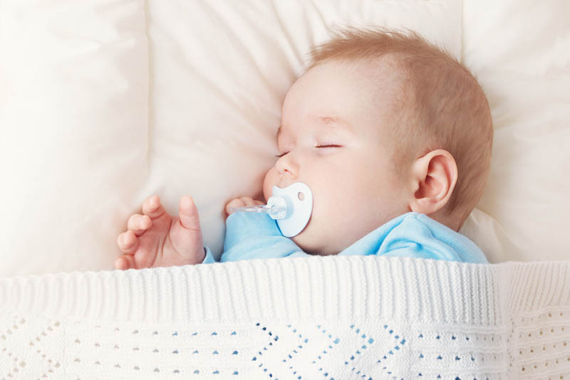 Baby schlafend mit Schnuller auf dem weißen Kissen mit Decke bedeckt