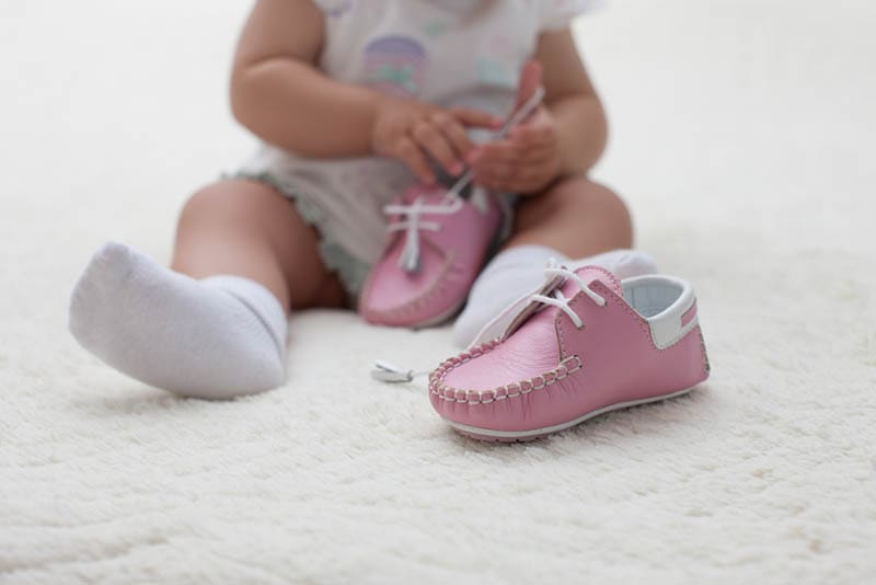Baby sitzt auf dem Boden und spielt mit rosa Schuhen