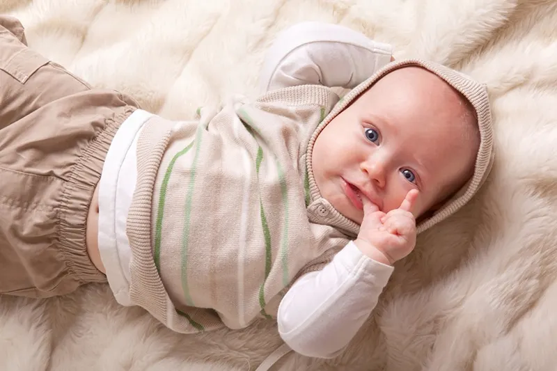 Baby trägt Pullover mit Hut und saugt Daumen auf dem Bett