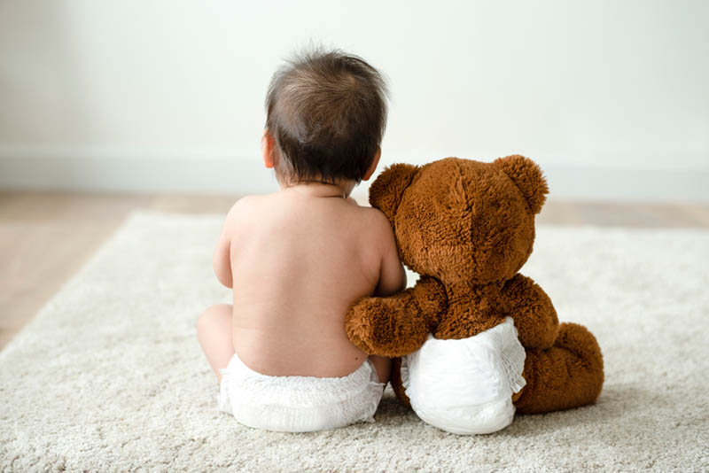 Baby trägt Windel sitzt auf dem Boden mit einem Teddybär auch in Windel