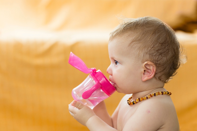 Baby trinkt Wasser und trägt Bernsteinkette