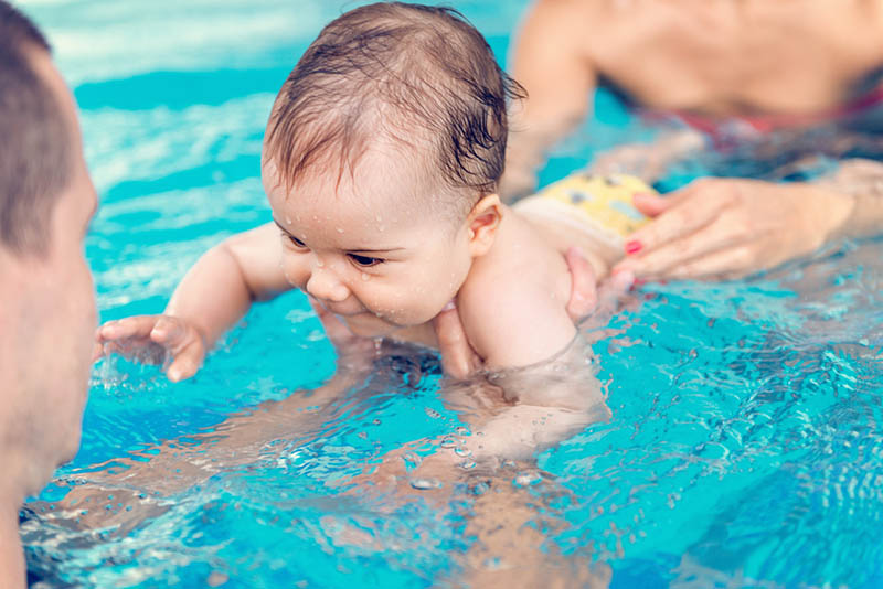 Eltern, die sich im Pool vergnügen und dem Baby das Schwimmen beibringen