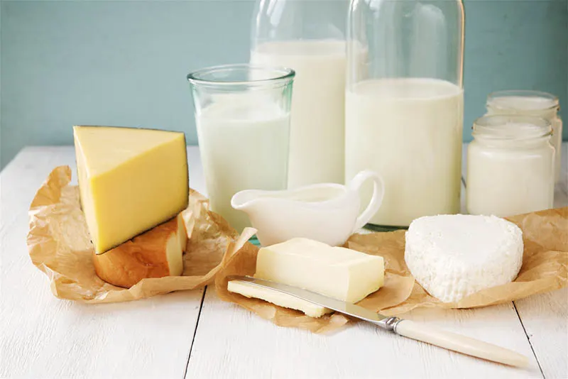 Flaschen mit Milch und Gläser mit Joghurt und Käse auf dem weißen Holztisch