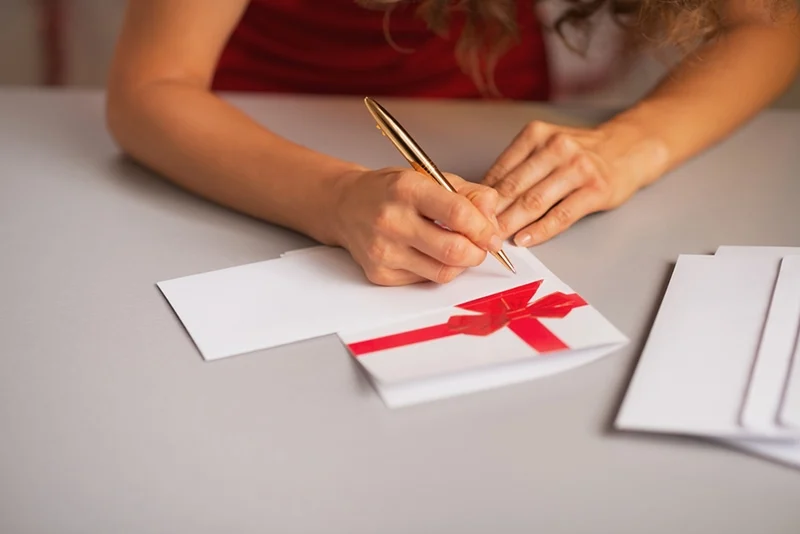Frau mit lockigem Haar sitzt am Tisch und schreibt einen Brief