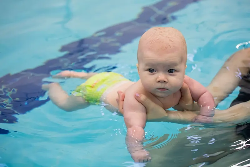 Glückliches Babybaby, das das Schwimmen im Pool genießt, der von Mutter gehalten wird