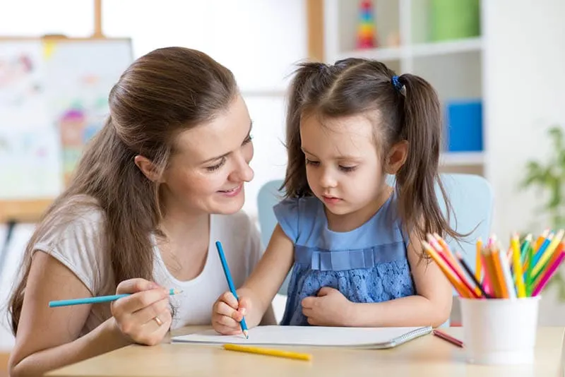 Junge Lehrerin Zeichnung zusammen mit niedlichen kleinen Mädchen im Kindergarten