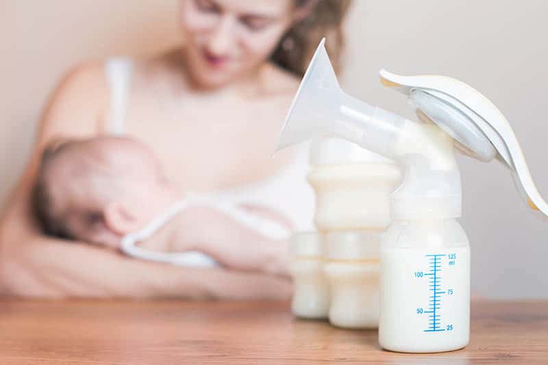 Mutter hält Baby mit Milchpumpe und einer Milchflasche auf dem Tisch vor