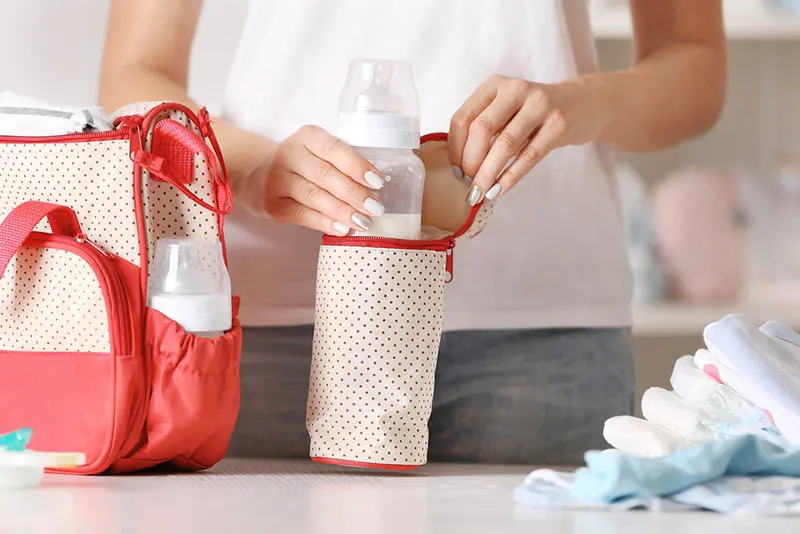 Mutter packt Babymilchflasche in die Tasche für Wickeltasche