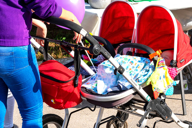 Mutter zu Fuß und schieben Babys in den Zwillingskinderwagen im Freien auf den sonnigen Tag