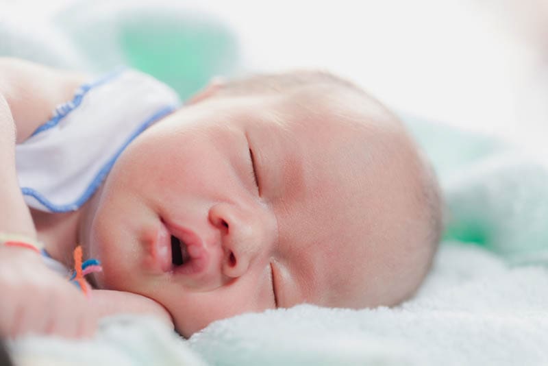 Neugeborenes Baby schlafend im Bett mit offenem Mund