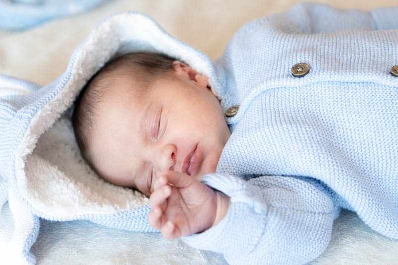 Neugeborenes Baby trägt eine warme blaue Jacke mit Spielzeug Hasenohren schlafen auf Decke