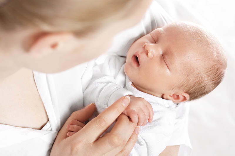 Neugeborenes, das mit offenem Mund in den Händen der Mutter schläft