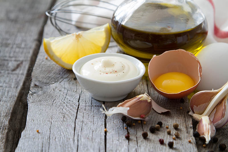 Schale mit Mayonnaise und Zitrone, Knoblauch und Olivenöl auf dem Holztisch