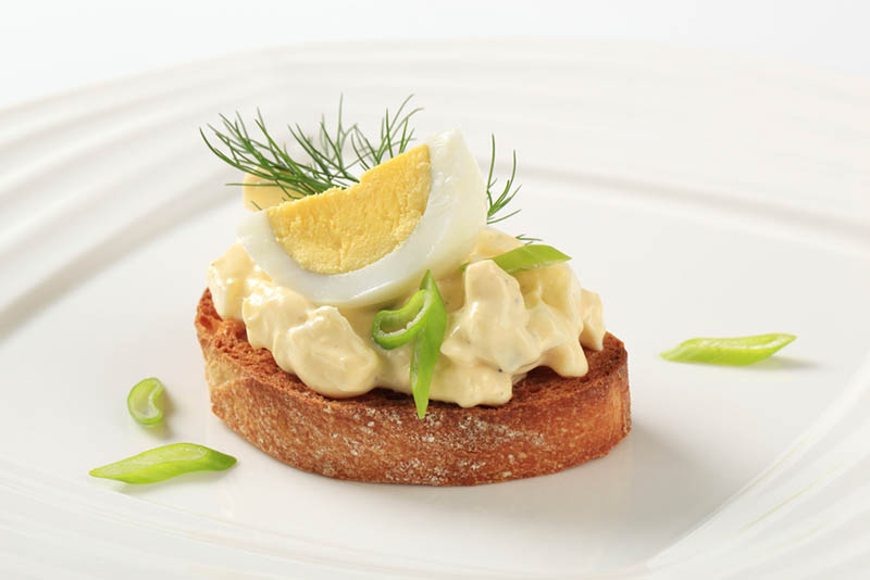 Scheibe Toastbrot mit Mayonnaise und einem Ei mit Gewürzen, serviert auf dem weißen Teller