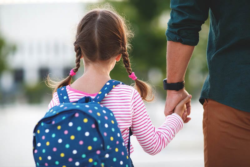 Vater führt seine kleine Tochter mit Rucksack zur Schule