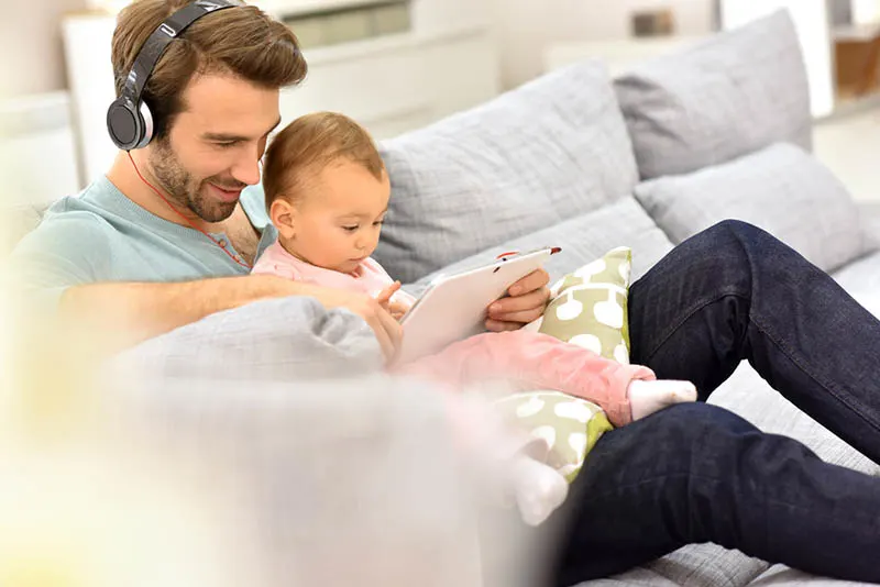 Vater sitzt mit Baby auf der Couch und hört Musik mit Kopfhörern