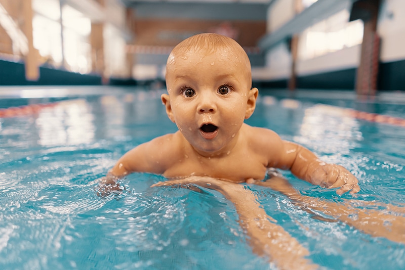 aufgeregtes Baby, das lernt, im Pool zu schwimmen