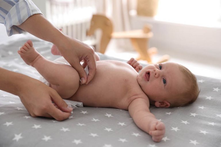 Mutter wechselt Windel zu Baby auf dem Bett zu Hause
